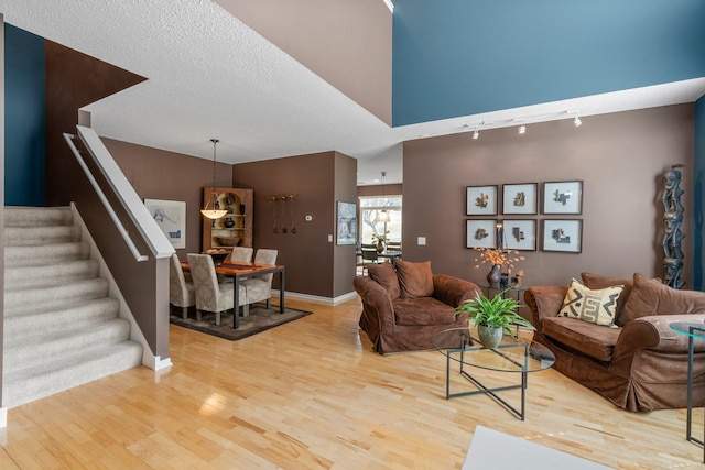 living area with track lighting, light wood-style flooring, baseboards, and stairway