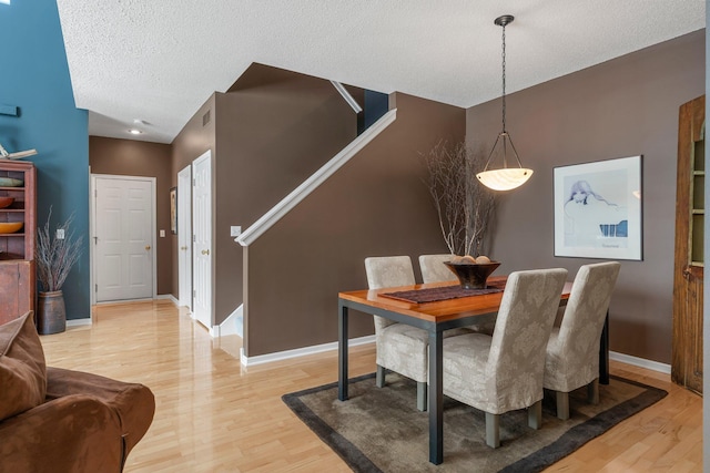dining area featuring baseboards, a textured ceiling, and light wood finished floors