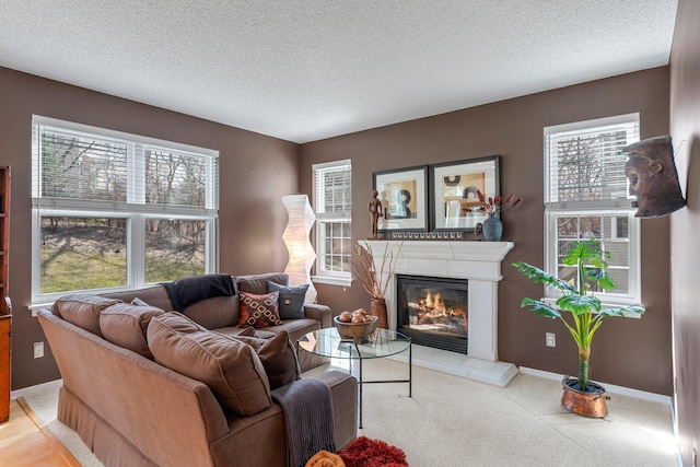 living room with a glass covered fireplace, a wealth of natural light, a textured ceiling, and light colored carpet