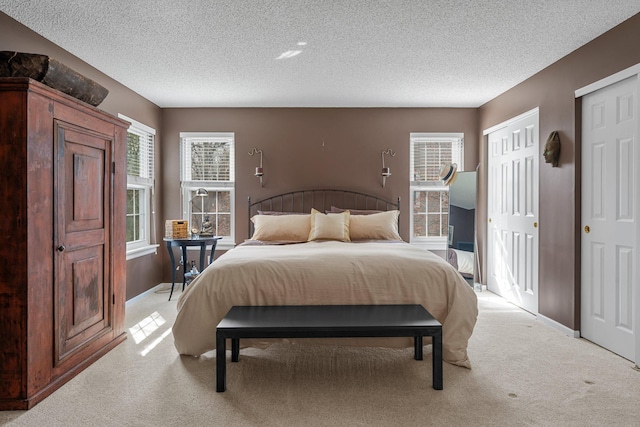 bedroom with two closets, a textured ceiling, and light carpet