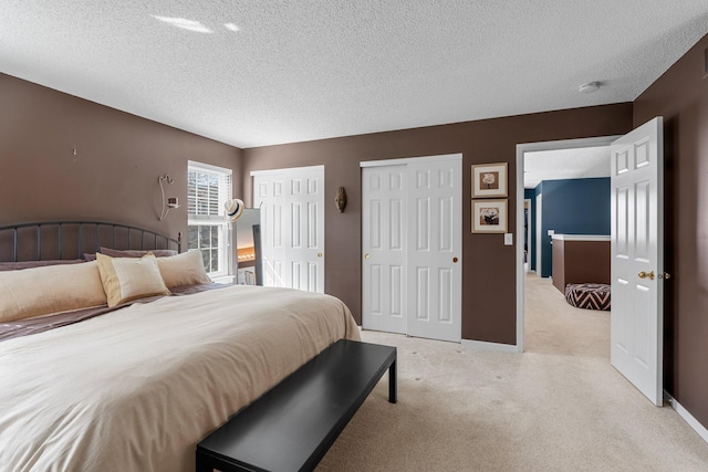 bedroom with multiple closets, a textured ceiling, and light colored carpet