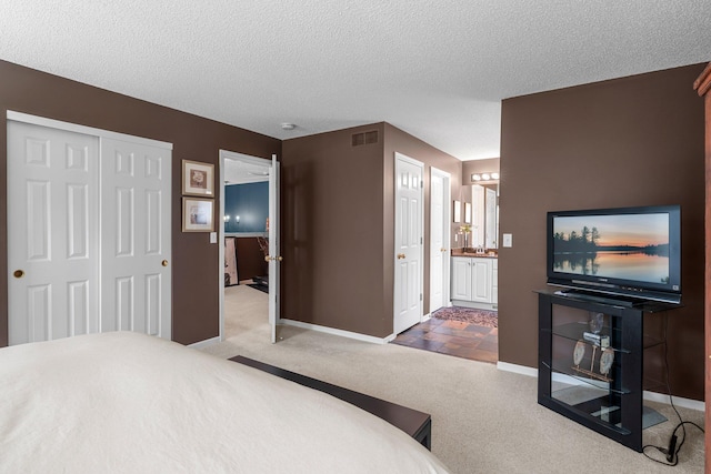 carpeted bedroom featuring a textured ceiling, visible vents, baseboards, a closet, and ensuite bath
