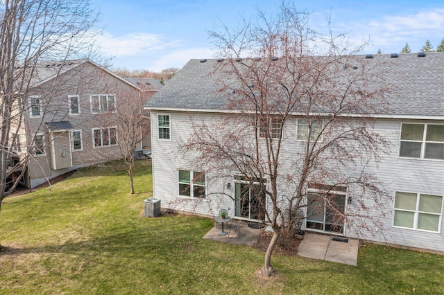 rear view of property featuring a lawn, central AC unit, roof with shingles, and a patio area