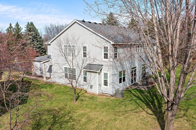 back of house with roof with shingles and a yard