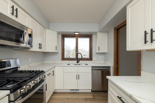 kitchen featuring white cabinets, a sink, light wood-style floors, light stone countertops, and appliances with stainless steel finishes