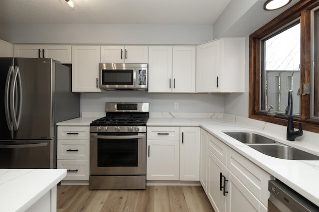 kitchen with light stone counters, light wood-style floors, stainless steel appliances, and a sink