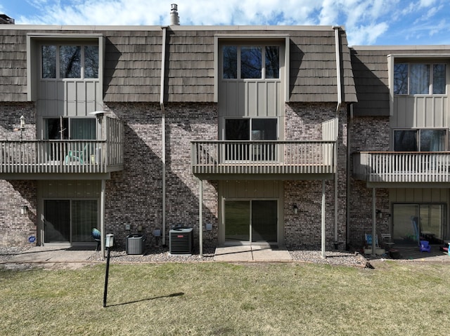 back of property with a lawn, brick siding, mansard roof, and a balcony