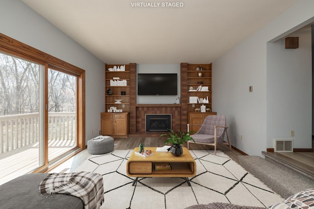 living area featuring a brick fireplace, light wood-style floors, and visible vents