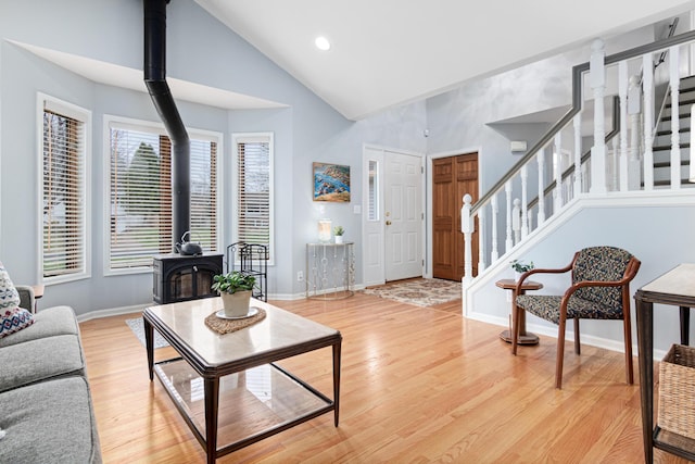 living room with a wood stove, high vaulted ceiling, baseboards, wood finished floors, and stairway