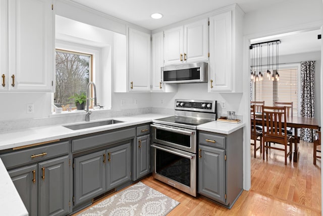 kitchen with a sink, gray cabinets, stainless steel appliances, and white cabinets