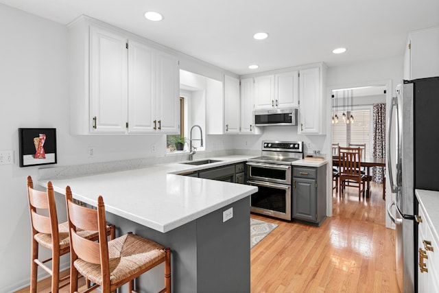 kitchen with a peninsula, a sink, light wood-style flooring, appliances with stainless steel finishes, and gray cabinetry
