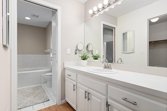 full bath with vanity, visible vents, wood finished floors, toilet, and tiled bath
