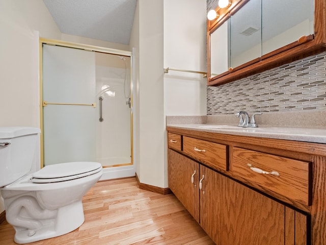 bathroom featuring backsplash, wood finished floors, toilet, vanity, and a stall shower
