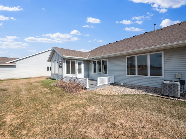 rear view of property featuring roof with shingles, a yard, and central AC unit