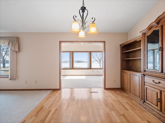 unfurnished dining area with visible vents, light wood-style flooring, baseboards, and an inviting chandelier