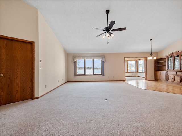 unfurnished living room featuring carpet floors, lofted ceiling, baseboards, and ceiling fan with notable chandelier