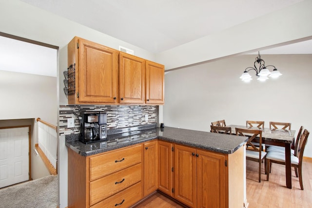 kitchen featuring decorative backsplash, a peninsula, light wood-style floors, a notable chandelier, and decorative light fixtures
