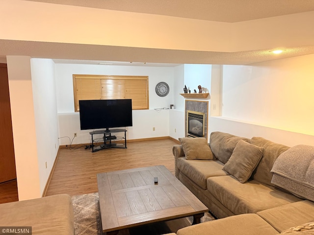 living area featuring baseboards, a tiled fireplace, and light wood-style floors