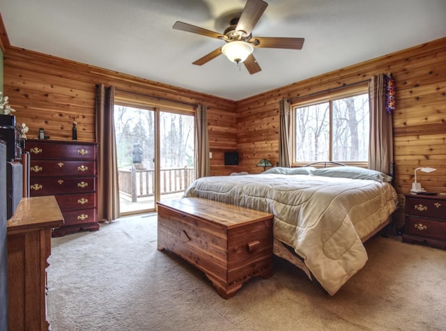 carpeted bedroom with ceiling fan, wood walls, access to exterior, and multiple windows