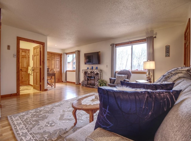 living area featuring a fireplace, a textured ceiling, baseboards, and light wood-style floors