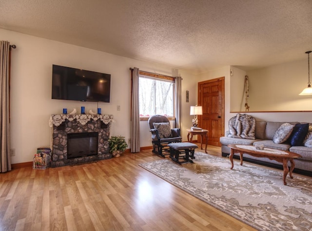 living room with baseboards, light wood-style flooring, a textured ceiling, and a fireplace