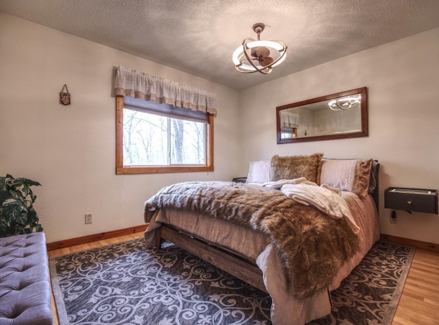 bedroom featuring an inviting chandelier, baseboards, a textured ceiling, and wood finished floors