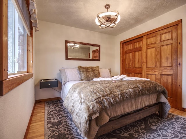 bedroom with baseboards, light wood-style flooring, a textured ceiling, and a notable chandelier