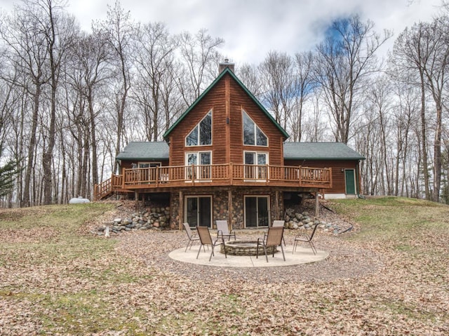 rear view of house featuring a chimney, a wooden deck, a patio area, a fire pit, and stone siding