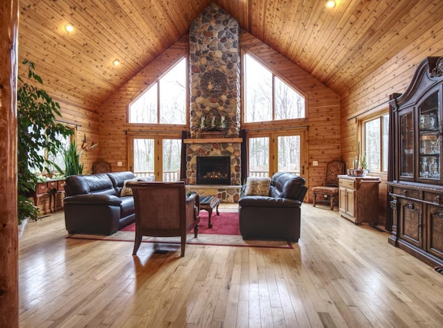 living room with a stone fireplace, wood walls, light wood-style flooring, and high vaulted ceiling