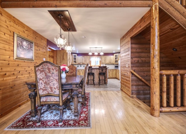 dining area with an inviting chandelier, wood walls, and light wood finished floors