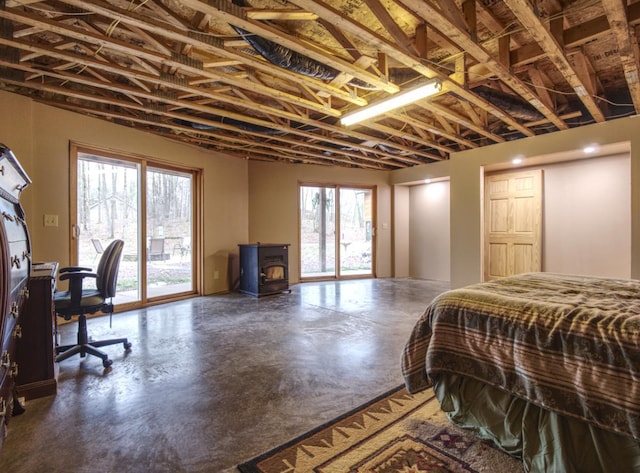bedroom featuring finished concrete floors, access to exterior, and a wood stove