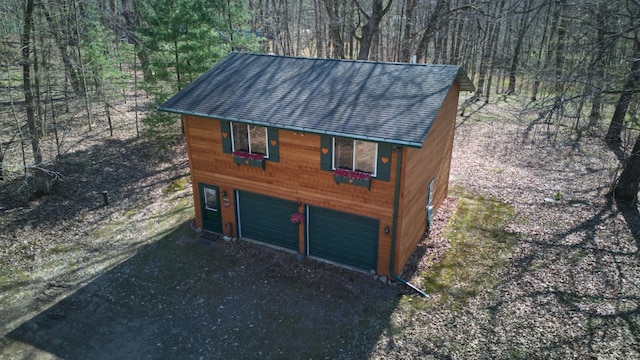 view of outdoor structure featuring driveway, a wooded view, and an attached garage