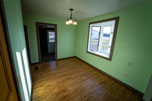 unfurnished room with baseboards, hardwood / wood-style flooring, visible vents, and a chandelier