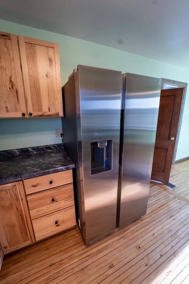 kitchen with light wood-style flooring, light brown cabinetry, dark stone counters, and stainless steel fridge with ice dispenser