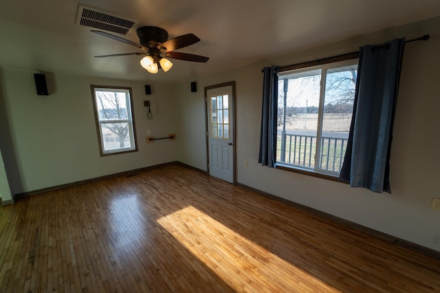empty room featuring a wealth of natural light, a ceiling fan, hardwood / wood-style floors, and visible vents
