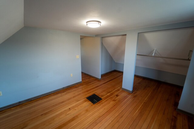 unfurnished bedroom with baseboards, hardwood / wood-style flooring, visible vents, and vaulted ceiling