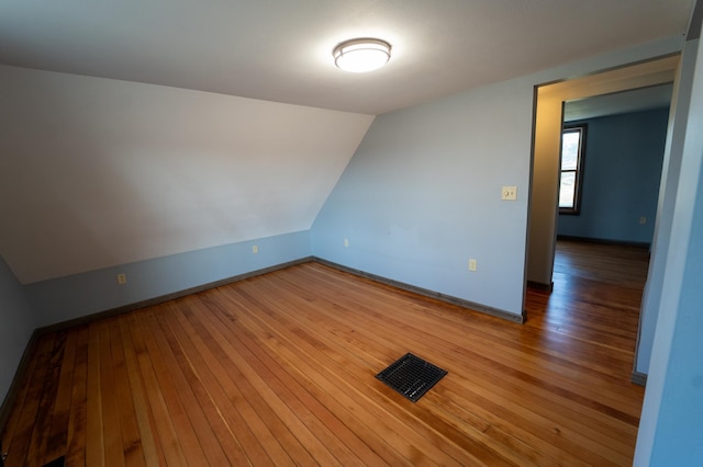 empty room with lofted ceiling, light wood-style floors, visible vents, and baseboards