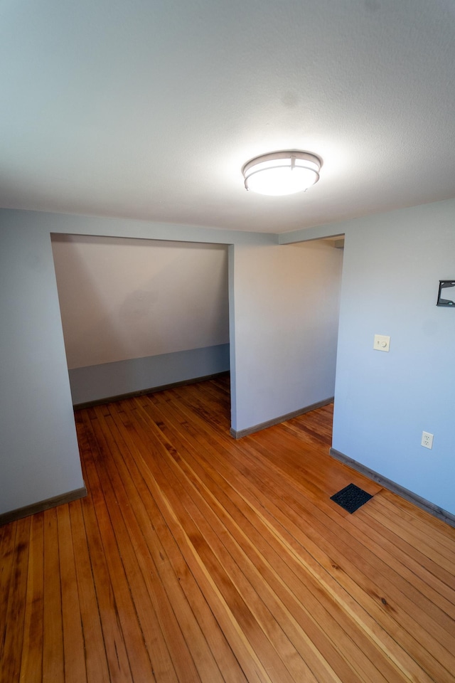 unfurnished room featuring baseboards, visible vents, and wood-type flooring
