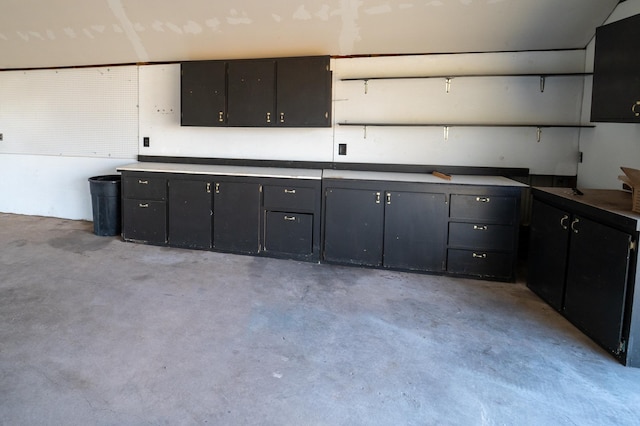 kitchen featuring open shelves, concrete flooring, and dark cabinets