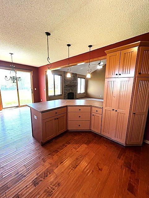 9521 Dunes Ct, Cottage Grove, MN 55016 - kitchen featuring dark wood-style flooring, a textured ceiling, a fireplace, a peninsula, and hanging light fixtures