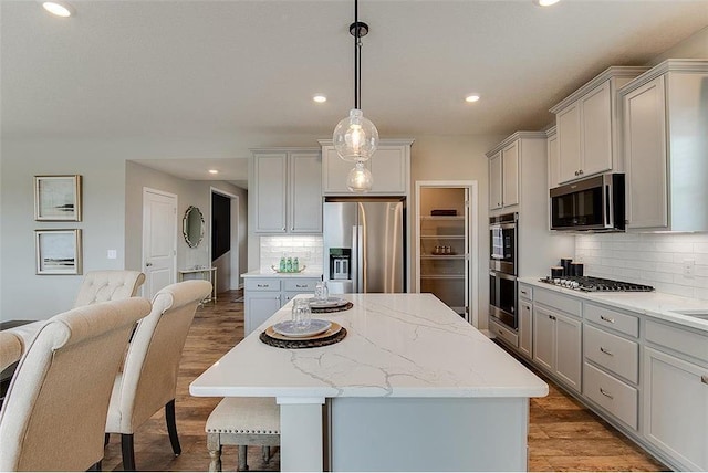 kitchen featuring stainless steel appliances, recessed lighting, backsplash, wood finished floors, and a kitchen island