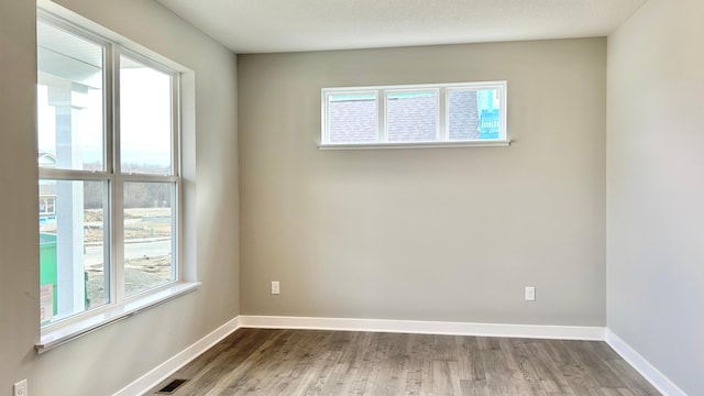 unfurnished room featuring baseboards, visible vents, and wood finished floors