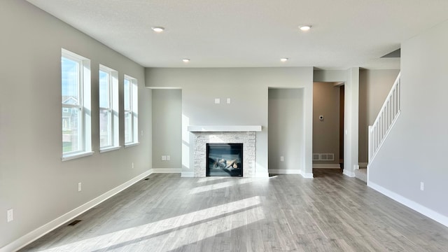 unfurnished living room featuring visible vents, baseboards, wood finished floors, and stairway