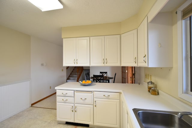 kitchen with a peninsula, light countertops, a sink, and white cabinetry