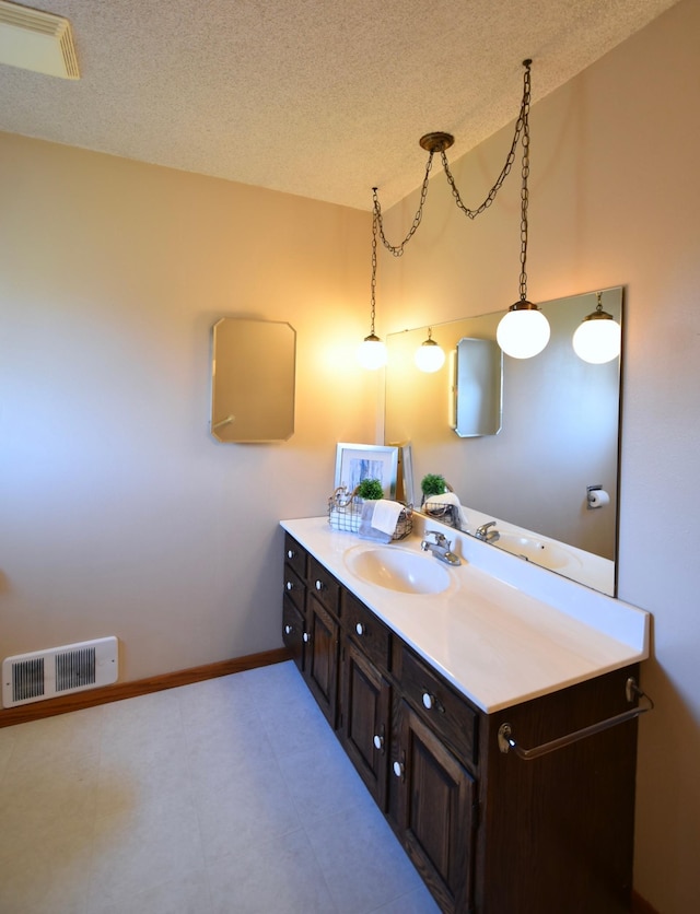 bathroom with baseboards, visible vents, a textured ceiling, and vanity