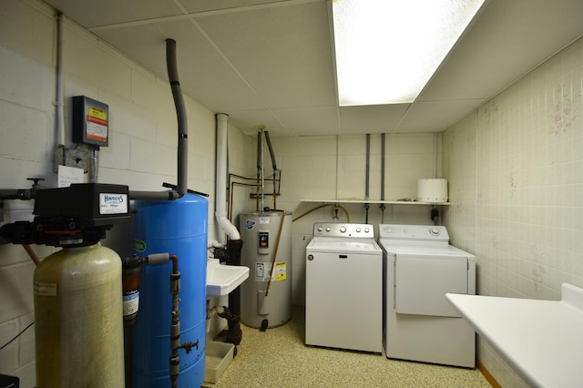 clothes washing area with concrete block wall, washing machine and dryer, water heater, and laundry area