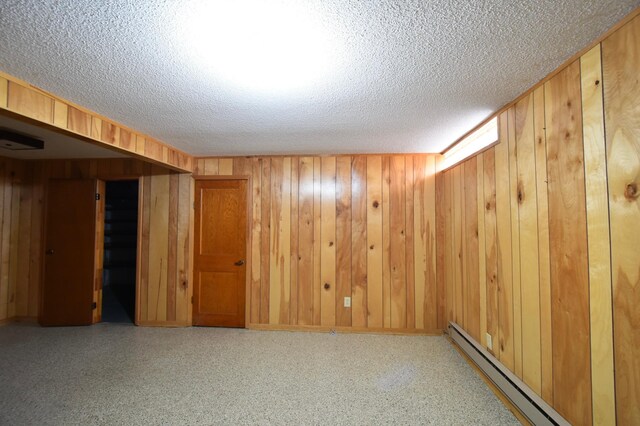 empty room with wood walls, a textured ceiling, and a baseboard radiator