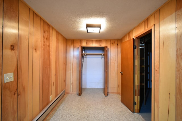 corridor with a baseboard radiator, a textured ceiling, and wood walls