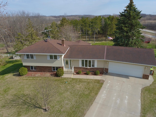 split level home with a chimney, concrete driveway, an attached garage, brick siding, and a front yard
