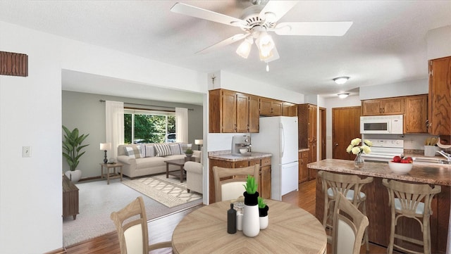 kitchen featuring light wood-type flooring, brown cabinets, a sink, and white appliances